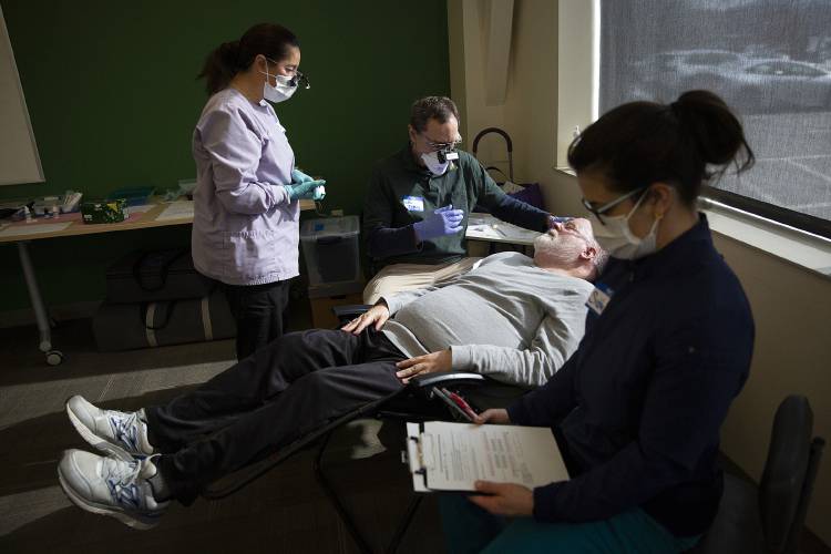 Dr. John Echternach, center, offers a second opinion to dental hygienists Lisa Watson, left, and Siobhan Nadler, right, as they decide whether a filling is needed for Earl Parker, of Windsor, Vt., during a free dental clinic at the Vermont Agency of Human Services Hartford District Office Building in White River Junction, Vt., on Friday, Feb. 9, 2024. The clinic offered cleanings as well as treatment of tooth decay with silver diamine fluoride and glass ionomer fillings, neither of which require drilling. (Valley News / Report For America - Alex Driehaus) Copyright Valley News. May not be reprinted or used online without permission. Send requests to permission@vnews.com.
