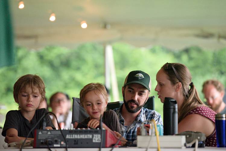 Hudson Fitch, 7, left, looks on as Corey Fitch and his wife Deanna Meadow, monitor their son Hayden Fitch, 5, as he operates the sound board during a party to for the 250th anniversary of their family farm in Cornish, N.H., on Saturday, July 29, 2023. The family lives on the farm with Corey's parents, Jim and Sue Fitch, who have stewarded the land for 40 years, and are reenvisioning it as a place for arts education. (Valley News - James M. Patterson) Copyright Valley News. May not be reprinted or used online without permission. Send requests to permission@vnews.com.