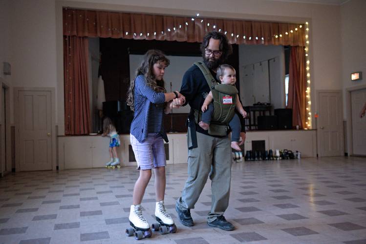 Kevin Lague, of Thetford, carries his youngest Mairenn, 9 months, and lends an arm to his daughter Gigi, 9, as she and her sister Gabby, 7, back left, try out roller skating during the fall festival at New Suns Community Center in North Thetford, Vt., on Friday, Sept. 6, 2024. (Valley News - James M. Patterson) Copyright Valley News. May not be reprinted or used online without permission. Send requests to permission@vnews.com.