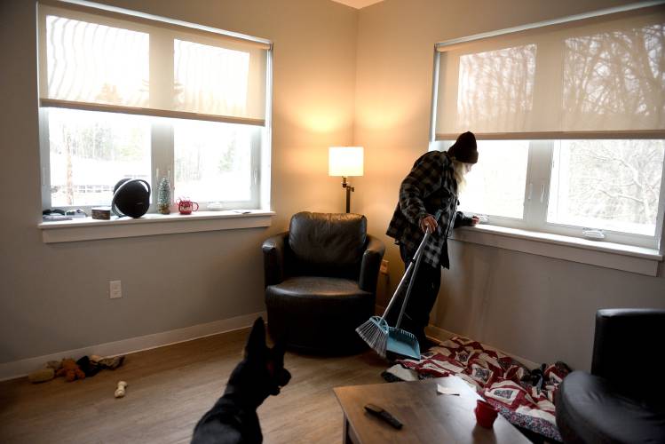 Charles Russo looks out his apartment window before taking his dog Eva out on Thursday, Dec. 19, 2024, in White River Junction, Vt. Russo has been disabled since falling 58 feet off of a roof. He moved into the apartment in October, one third of his social security check pays his rent. Developed by Twin Pines Housing, the 18 one-bedroom units are located on St. Paul’s Episcopal Church property, adjacent to the Upper Valley Haven.  (Valley News-Jennifer Hauck)