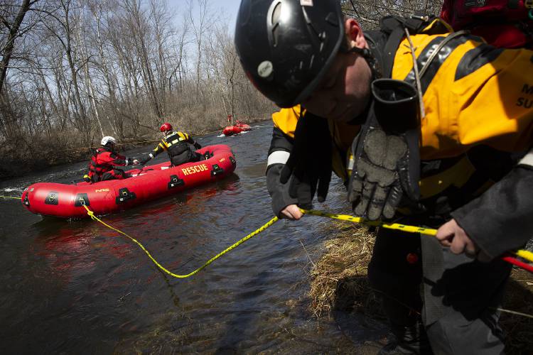 Hartford firefighter Will Heighes, right, lets out slack on a rope tethered to a rescue raft carrying Hanover firefighter Helder Ferreira, left, and Hartford firefighter Matt McCabe during a water rescue training scenario in the Mascoma River in Lebanon, N.H., on Wednesday, April 2, 2025. Members of the Lebanon, Hanover and Hartford fire departments participated in the training. (Valley News - Alex Driehaus)