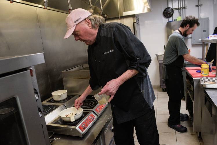 Chef Martin Murphy sautees garlic and chorizo on an induction range for gambas y chorizo in the Casa Brava Tapas Bistro's all-electric kitchen in Hanover, N.H., on Saturday, Dec. 14, 2024. Murphy, the former owner of Ariana's Restaurant, partnered with James Van Kirk, former owner of Candella Tapas Lounge to open Casa Brava this month. Sous chef Isaiah Johnson is at right. (Valley News - James M. Patterson) 