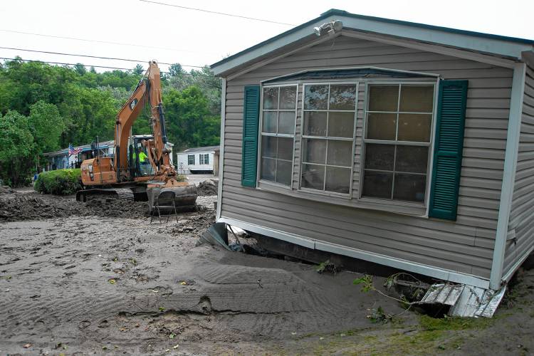 An excavator digs out access to a manufactured home that was flooded in Berlin on July 13, 2023. (VtDigger file - Natalie Williams)